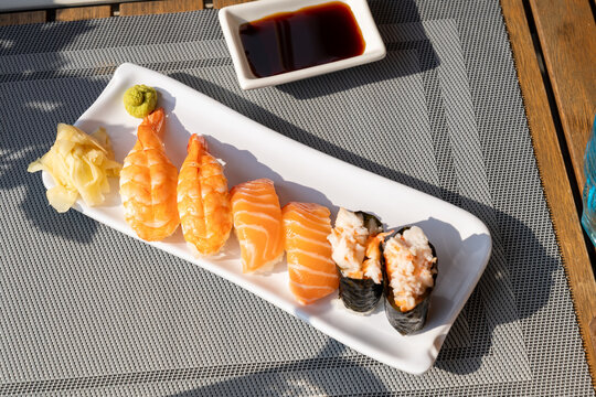 Assorted nigiri sushi on white platter in sunlight