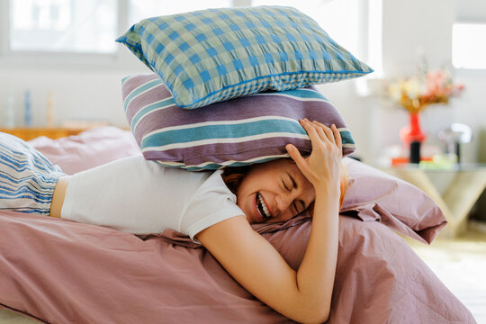 Woman laughing under stack of colorful pillows in bed