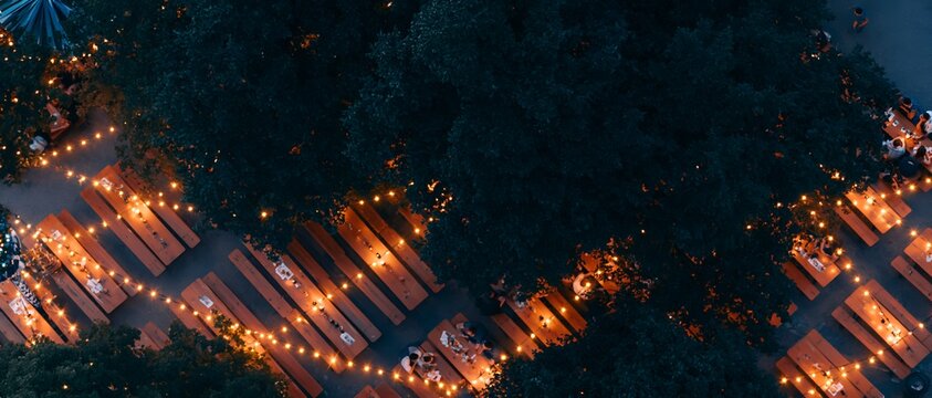 String lights decorate wooden tables under dark trees at night