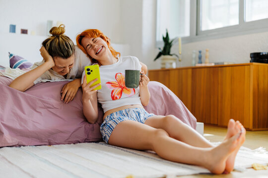 Women laughing at smartphone enjoying leisure time at home