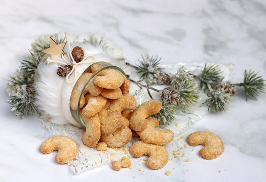 Traditional vanilla crescent cookies are arranged in a winter-themed glass jar against a light-colored marble background.