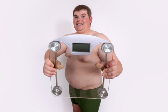 Fat man holds weighing scale. Large fat belly shows clearly. Fat body indicates overeating problem. Fat reduction needs healthy diet. Overweight man faces weight gain. Scale check overweight.