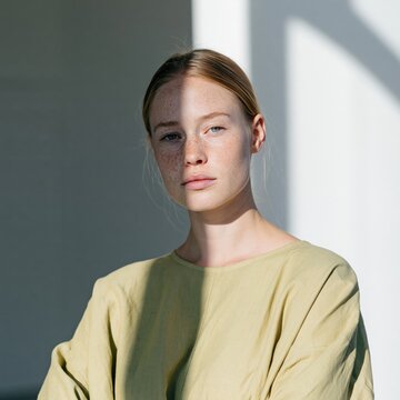 Minimal natural light portrait of a freckled woman with a pale green blouse and dramatic shadow for minimalist editorial and fashion banner