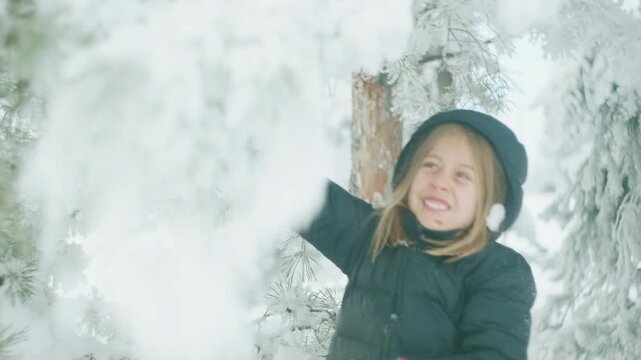 Close-up of a boy shaking snow-covered branches as a cascade of powder falls all around him