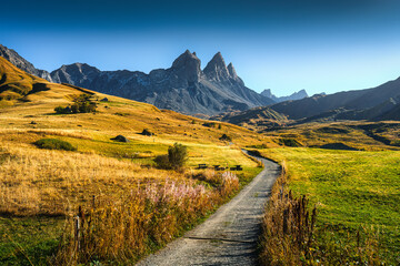 Fototapeta premium Winding gravel path through alpine valley with Aiguilles d Arves mountain peaks in French Alps during autumn
