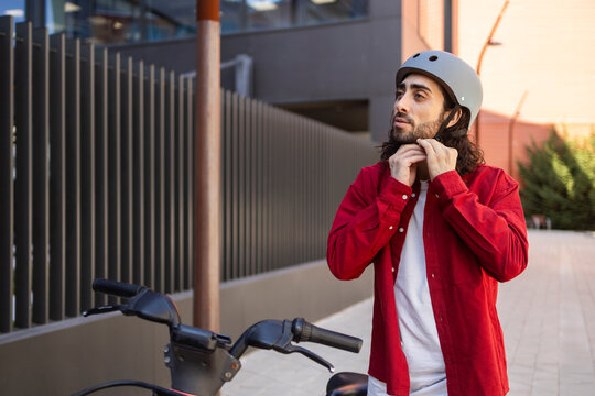 Man fastening helmet beside scooter in modern city