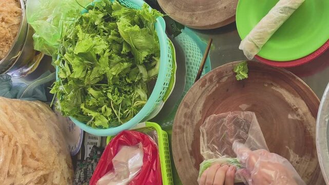 Top-down view of a vendor rolling traditional Central Vietnamese grilled pork spring rolls with fresh herbs