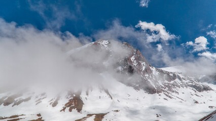 Broad snowy valley framed by rocky peaks and drifting clouds at Bogdanovich Glacier in the Ile Alatau mountain range. © Kolchanov