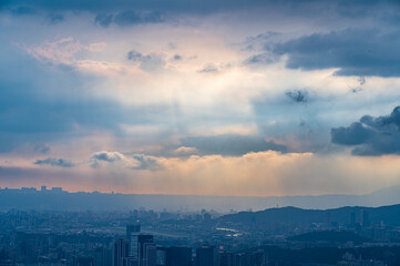 Fototapeta premium High angle aerial view of the Taipei city skyline and mountain ranges under dramatic dramatic sun rays and storm clouds in Taiwan.
