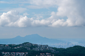 Fototapeta premium A breathtaking panoramic view from Mount Shizitou overlooking the sprawling cityscape and majestic mountain ranges under a cloudy blue sky in New Taipei City, Taiwan.