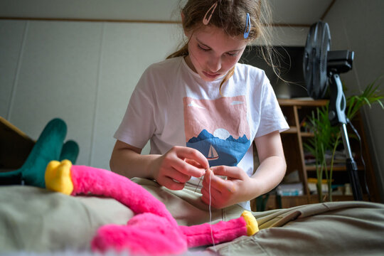 Focused preteen girl sewing and fixing her colorful plush toy at home
