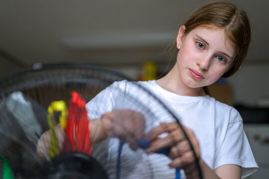 Thoughtful young girl playing with electric fan and ribbons at home