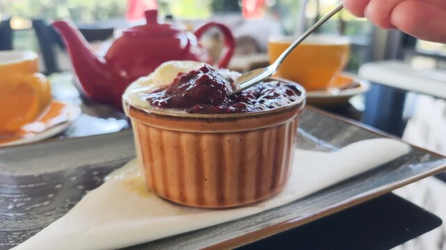 Spoon scoops delicious chocolate fondant topped with berry jam and vanilla ice cream in ceramic ramekin. Tasting sweet chocolate fondant during cozy teatime serving in cafe close up.