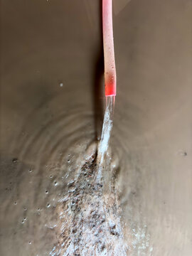 Clear Water Pours From Pink Hose Into Muddy Water Creating Ripples