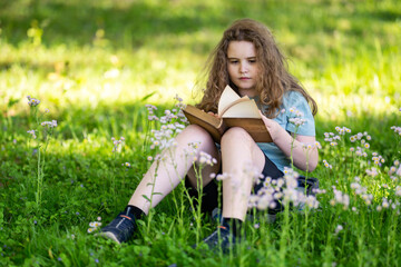 Fototapeta premium Child reading book in blurred bokeh. Young child enjoys reading book quietly. Educational portrait shows child reading book. Summer nature surrounds peaceful reading book.