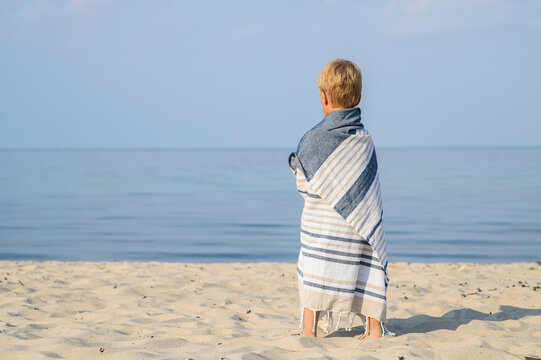 Young Boy Wrapped in Striped Beach Towel Looking at Calm Water