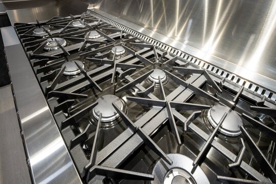 Close-up view of a professional stainless steel gas stove cooktop with heavy-duty black cast iron grates and multiple burners.