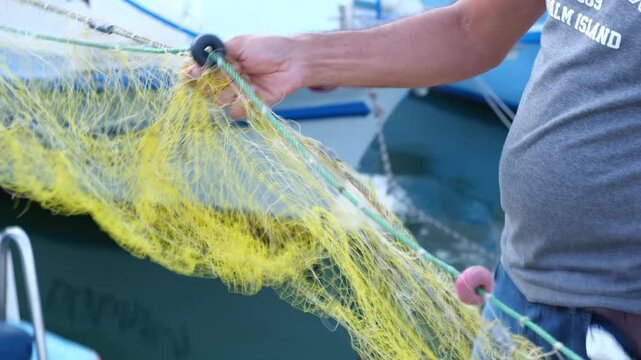 A detailed close-up video of a fisherman's weathered hands carefully sorting, mending, and pulling a nylon fishing net. Captured in authentic natural light, showcasing traditional craftsmanship, hard 