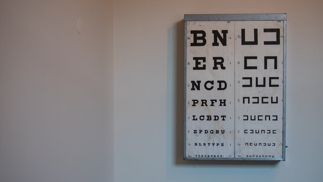 Vintage Snellen Eye Test Chart with Letters and Landolt C Symbols Mounted on a Plain Wall &mdash; Optometry, Vision Testing and Eye Health Concept