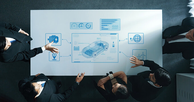A diverse business team engages in a strategy session, analyzing automotive technologies displayed on a digital interface in a modern office setting. Trope