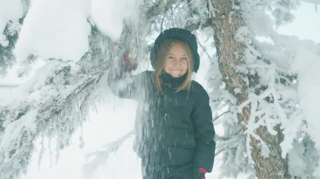 Boy smiling directly at the camera as snow falls around him after shaking a tree branch
