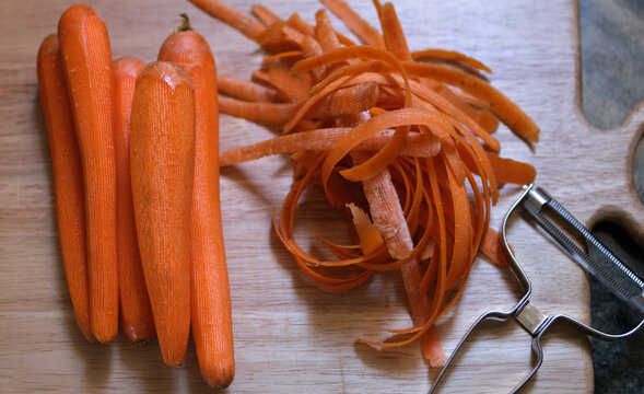 Top view of peeled carrots with vegetable peels and a vegetable peeler on a kitchen surface