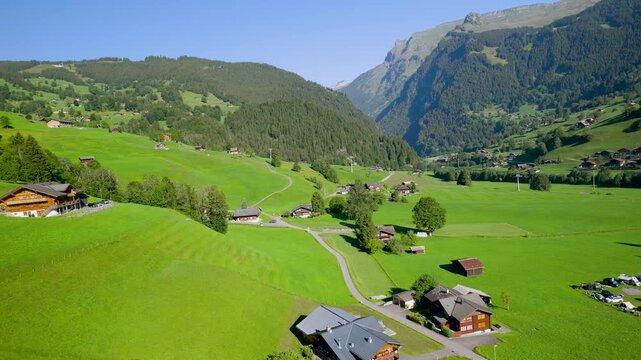 Idyllic aerial shot of a stunning green valley with traditional swiss chalets and mountains. Switzerland