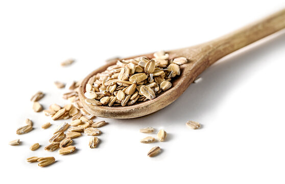 Wooden spoon heaped with raw oats and scattered oat flakes on white background closeup,
