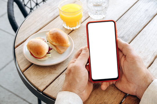 Mockup man's hand holding using smart phone with white blank screen POV at coffee shop, mobile app design and advertising, online marketing	