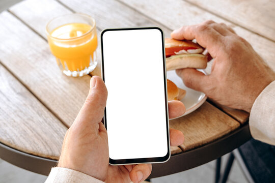 Mockup man's hand holding using smart phone with white blank screen POV at coffee shop, mobile app design and advertising, online marketing	