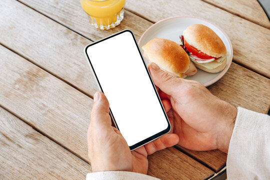 Mockup man's hand holding using smart phone with white blank screen POV at coffee shop, mobile app design and advertising, online marketing	
