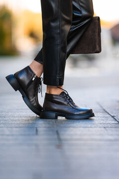 Black leather boots with matching pants and textured bag in urban street style, glossy surfaces, close detail, sunset light, bold fashion mood, polished stitching and modern city look