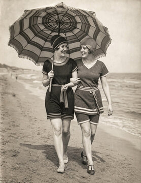 Two women in 1920s swimsuits under beach parasol