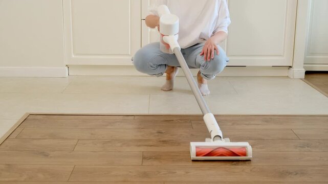 Woman cleaning floor with cordless vacuum cleaner. Housekeeper tidying kitchen interior. Maintenance of home hygiene and sanitation. Modern lifestyle and apartment daily routine concept.