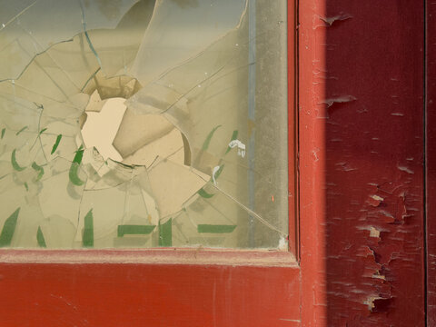 Broken window on an old weathered red door with pealing paint