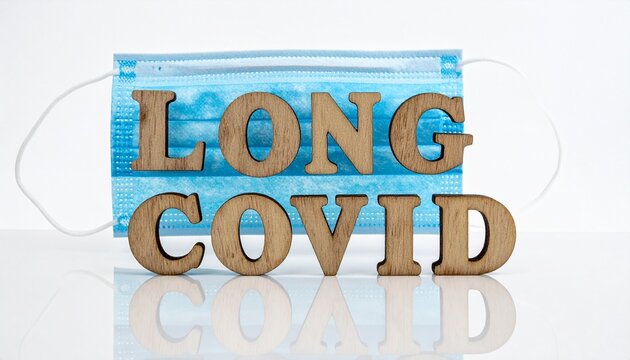Minimalist white background with wooden letters spelling LONG COVID placed before blue disposable face mask, symbolizing lingering pandemic health concerns.