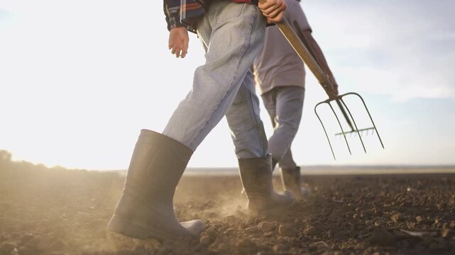 Farmer walk ground pitchforks. A boy and a man walk across the dusty field. The boy and the man hold a pitchfork, highlighting their work in the vast farmland.