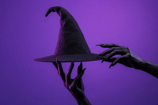 Creepy witch hat held by black monster hands on purple Halloween background
