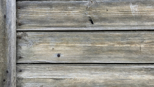 Close‑up of weathered wooden planks with pronounced grain patterns, knots, rusted nail heads, and aged gray tones, creating a rustic natural wood texture background with strong linear detail.