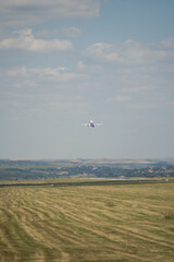 Passenger airplane flies in cloudy sky above green fields and horizon. Modern airliner ascent represents air travel commercial flight and global transport concept. © Tetiana