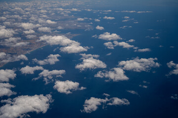 Fototapeta premium White fluffy cumulus clouds scattered over deep blue sea water aerial view. Freedom of travel and aviation transit concept in bright daylight environment.