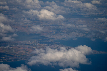 Fototapeta premium High angle aerial view of coastal terrain partially covered by white clouds. The image represents air travel, aviation, and planet surface observation.
