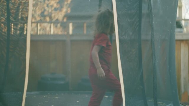 Boy standing on a backyard trampoline filmed through the safety net enclosure