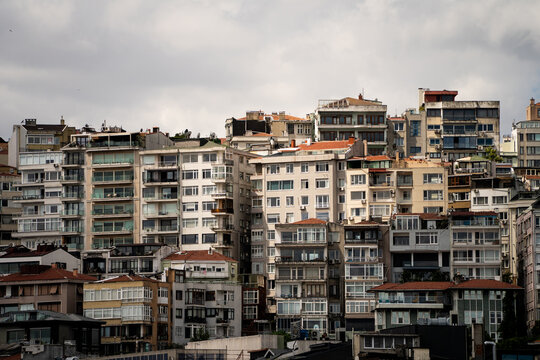 Multistory residential apartments sit densely packed along a steep hillside under an overcast sky. High density housing illustrates urban overpopulation and real estate expansion in coastal cities.