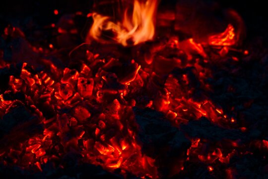 Glowing red coals with active fire flames close up campfire background