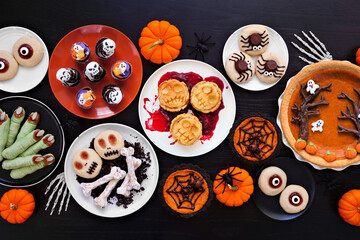 Fototapeta premium Fun Halloween dessert table scene over a black wood background. Overhead view. Variety of cookies, cupcakes and pumpkin and apple tarts and pies.