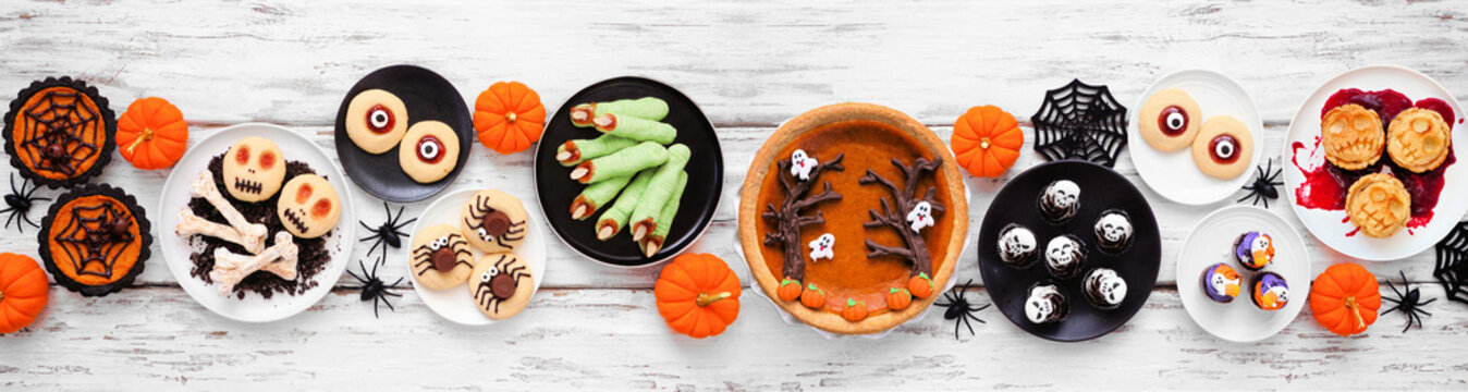 Fun Halloween dessert table scene over a white wood banner background. Top view. Variety of cookies, cupcakes and pumpkin and apple tarts and pies.