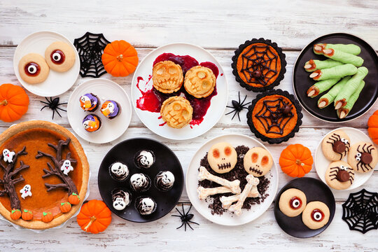 Fun Halloween dessert table scene over a white wood background. Above view. Selection of cookies, cupcakes and pumpkin and apple tarts and pies.