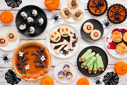 Fun Halloween dessert table scene over a white wood background. Above view. Variety of cookies, cupcakes and pumpkin and apple tarts and pies.
