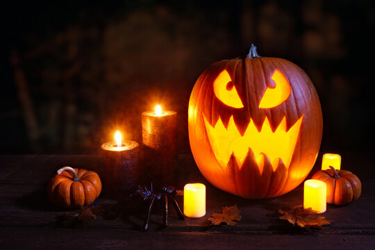 Halloween night scene with jack o lantern, pumpkins, candles and spider on a spooky dark background